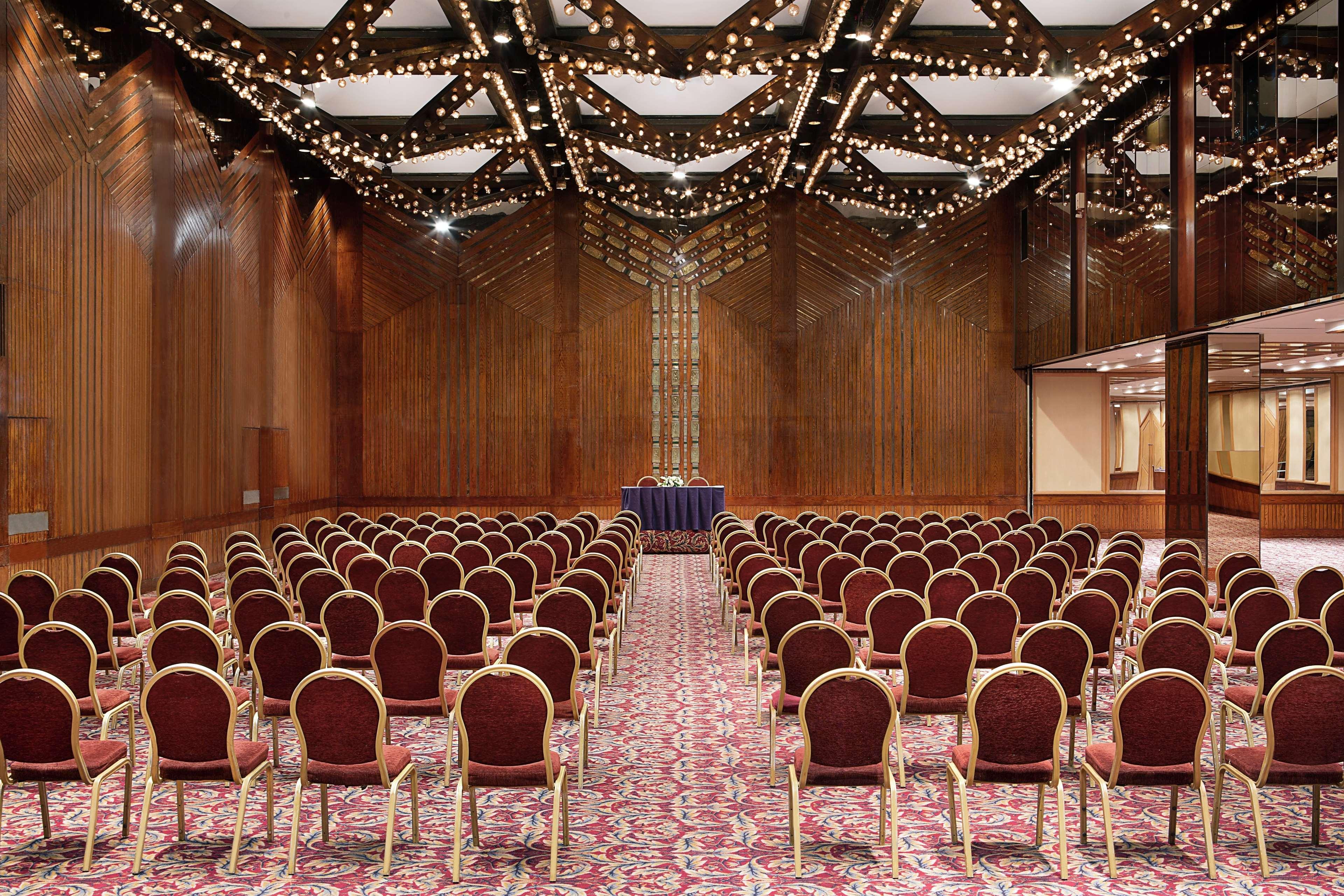 Ramses Hilton Hotel & Casino Kairo Exteriör bild The photo shows a spacious conference room or event hall. It features rows of burgundy chairs arranged neatly facing a small stage or podium at the front. The flooring is covered with an ornate patterned carpet, and the walls are made of polished woo