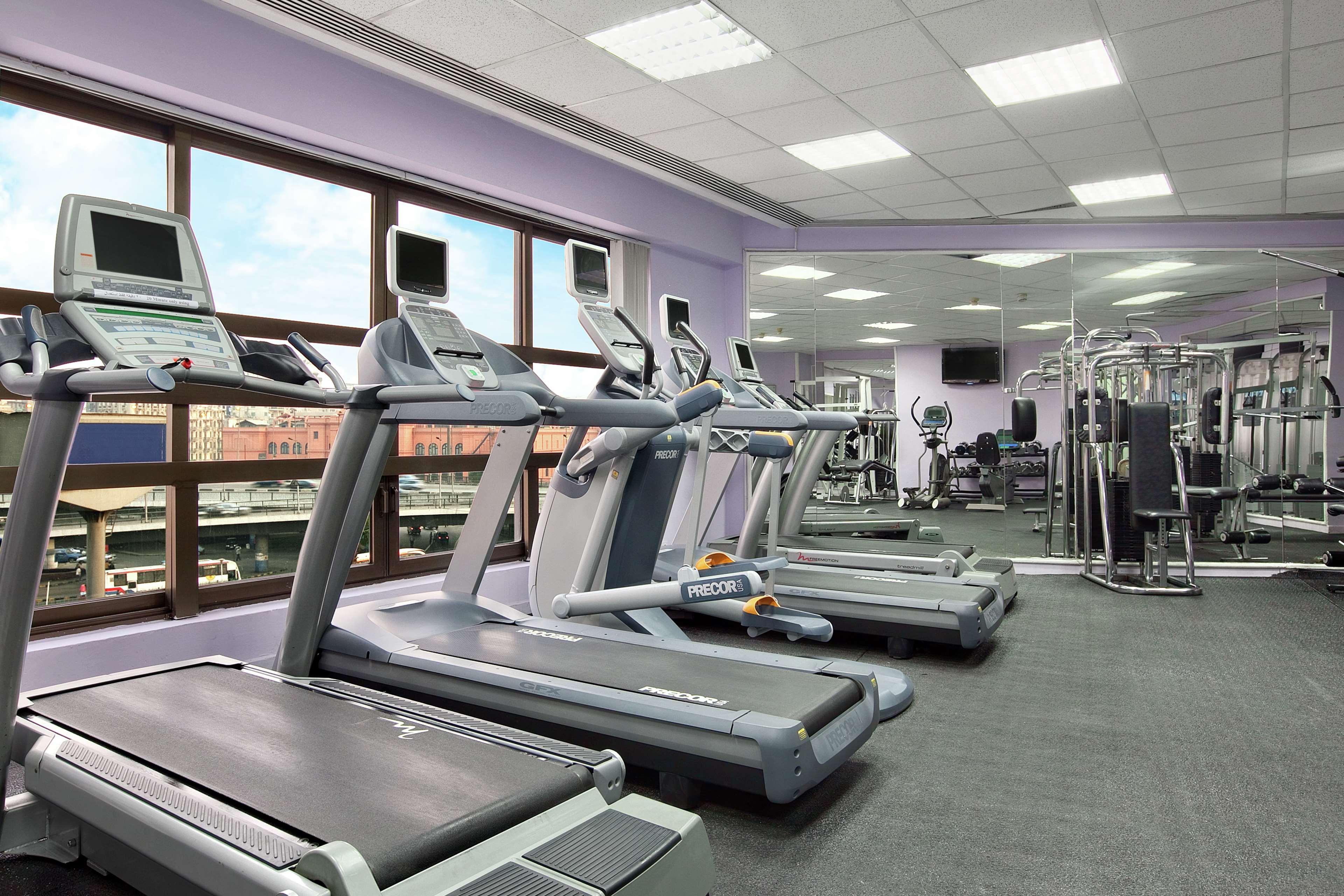 Ramses Hilton Hotel & Casino Kairo Exteriör bild The photo shows a modern gym or fitness center. There are several treadmills lined up in the foreground, with monitors on each one. The walls are painted in a light purple color, creating a bright and inviting atmosphere. In addition to the treadmill