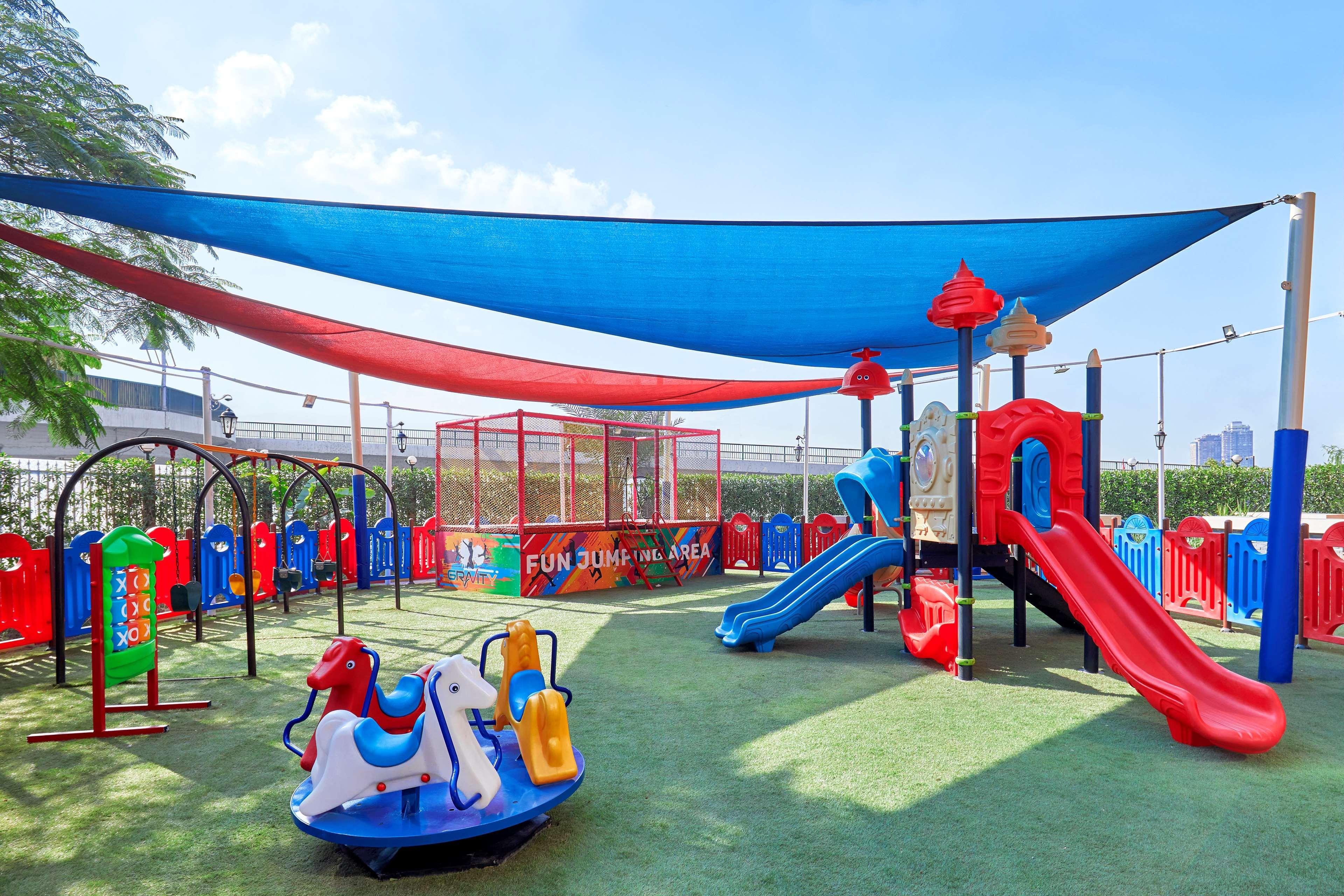 Ramses Hilton Hotel & Casino Kairo Exteriör bild The photo shows a colorful children's playground. It features various play structures, including two slides, swings, and a spring rider shaped like a horse. The area is covered with shade sails in blue and red, providing protection from the sun. Ther