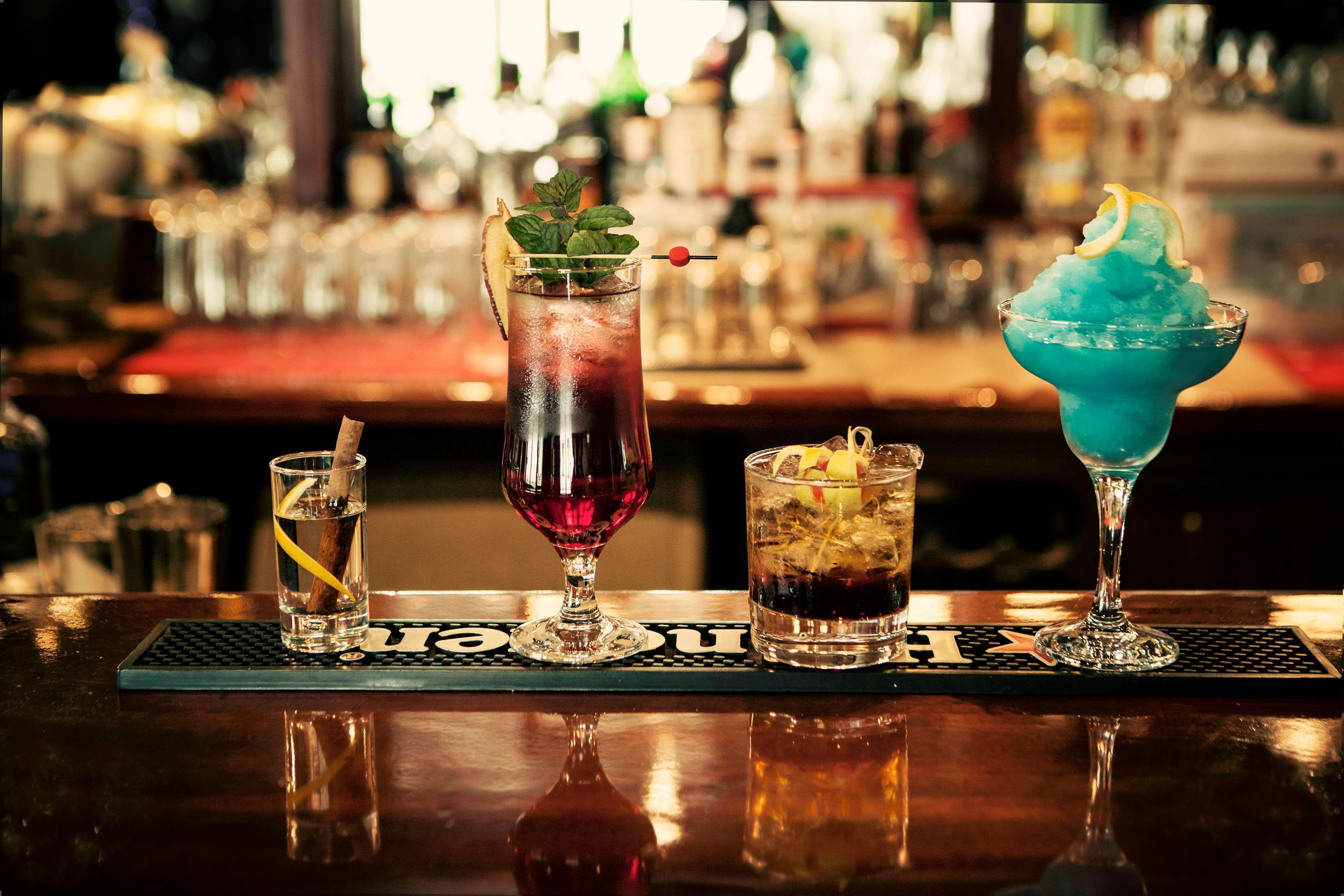 Ramses Hilton Hotel & Casino Kairo Exteriör bild The photo features a selection of four colorful cocktails arranged on a bar counter. From left to right:

1. A shot glass with a lemon twist, likely containing a clear spirit.
2. A tall glass cocktail, possibly a highball or a spritz, with a vibrant 