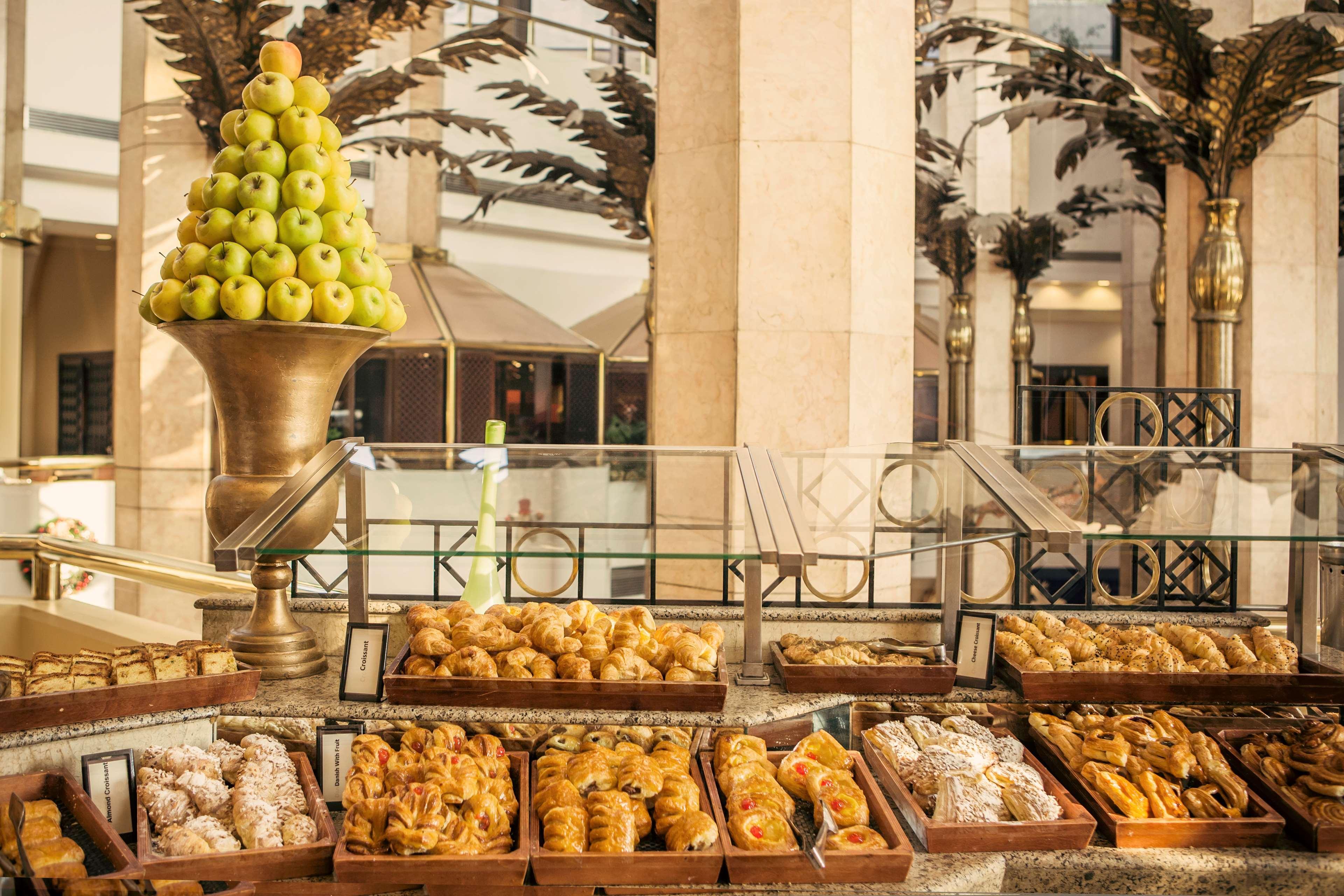 Ramses Hilton Hotel & Casino Kairo Exteriör bild The photo shows a lavish display of assorted pastries arranged on tables. Prominently featured is a decorative pedestal with a tall arrangement of green apples on top. Surrounding this centerpiece are various trays filled with an array of baked goods