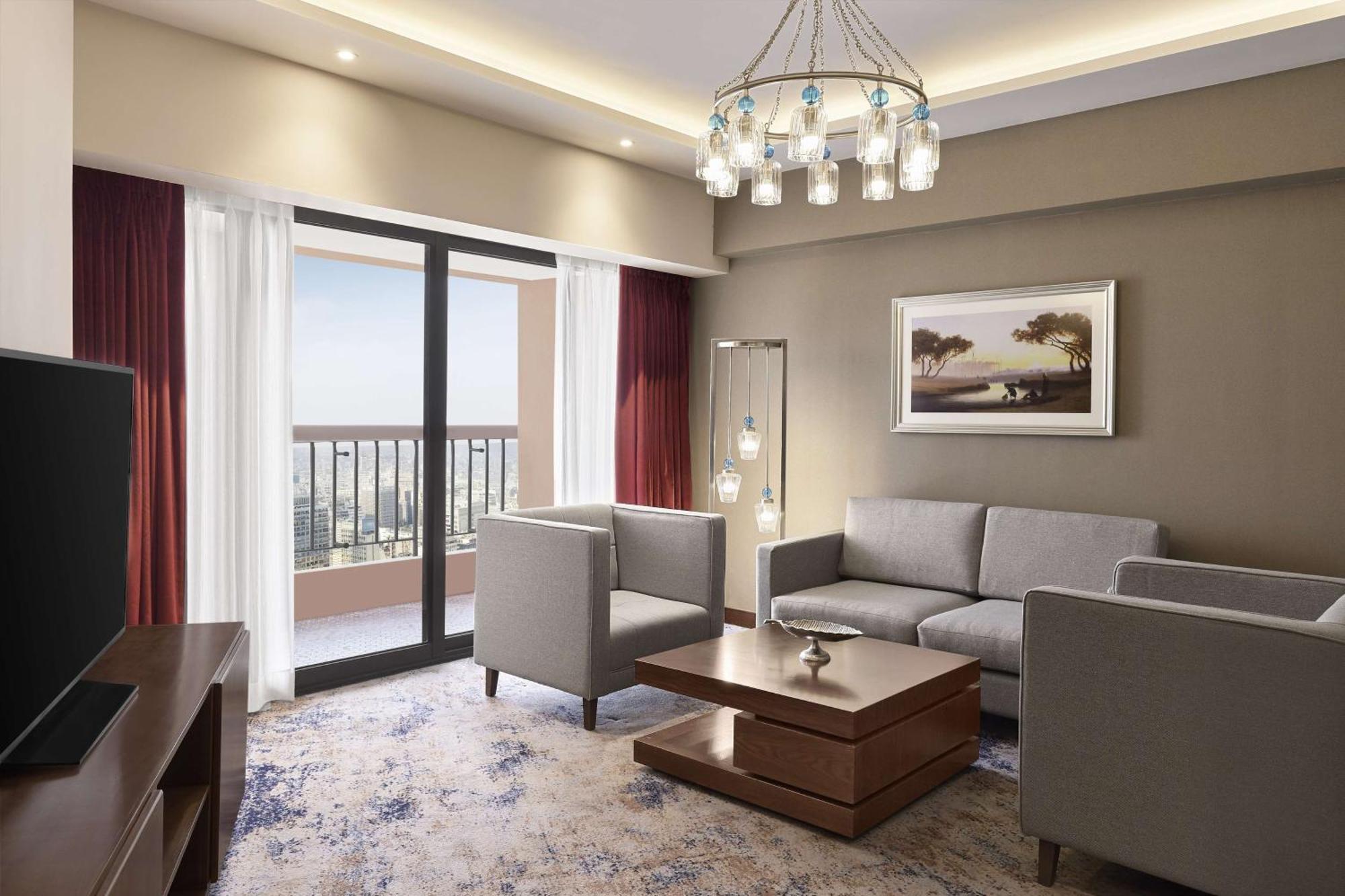Ramses Hilton Hotel & Casino Kairo Exteriör bild The photo depicts a modern living room in a well-designed space. It features a comfortable seating arrangement with two light-colored armchairs and a gray sofa positioned around a wooden coffee table. The walls are painted in neutral tones, and large